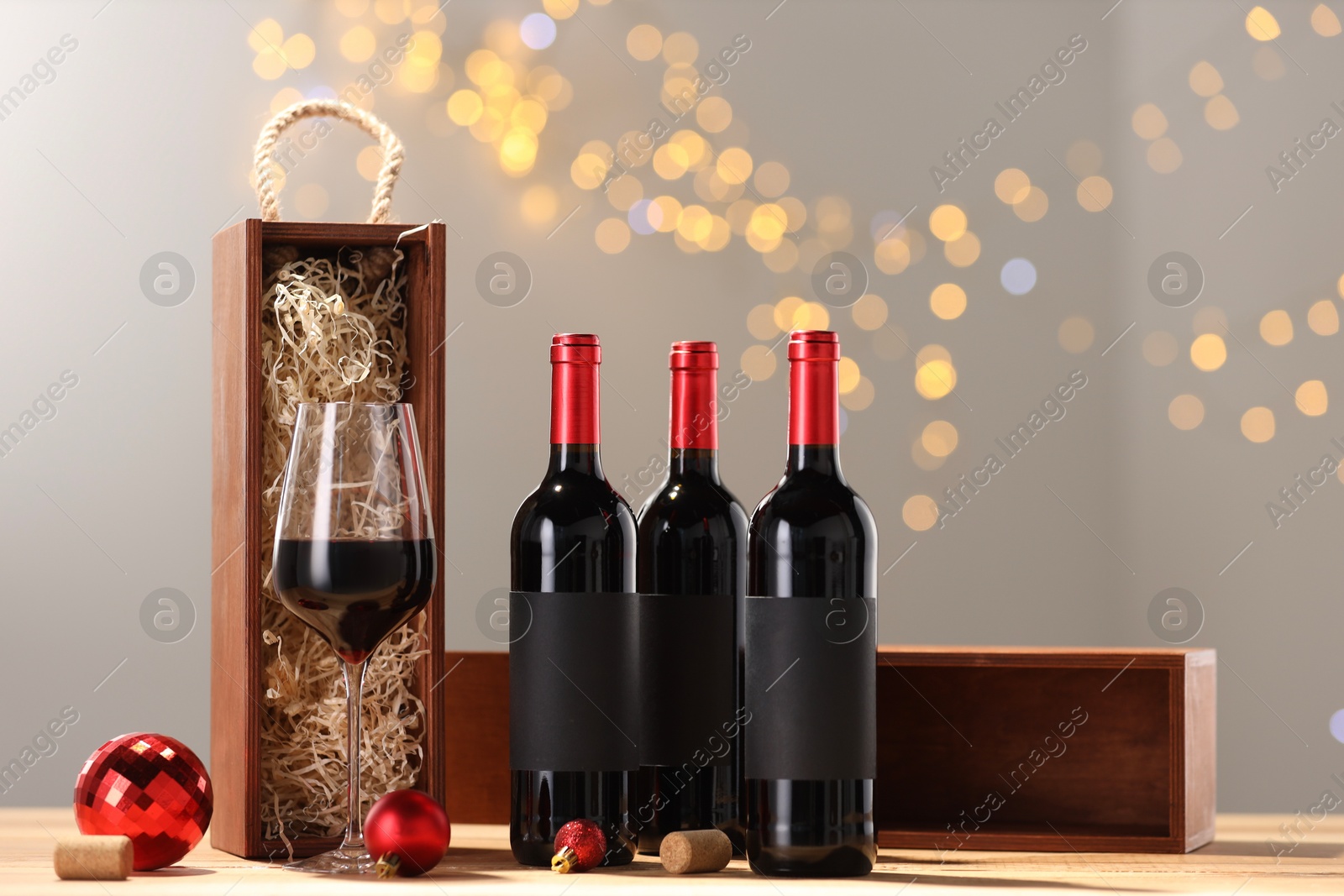 Photo of Bottles of wine, glass, wooden gift boxes, corks and red Christmas balls on table