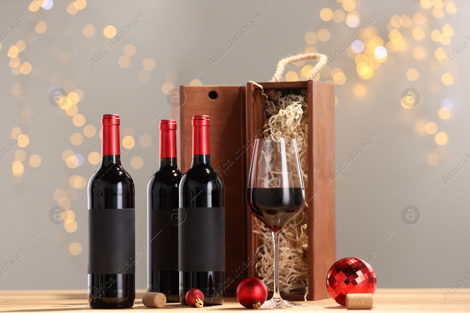 Photo of Bottles of wine, glass, wooden gift boxes, corks and red Christmas balls on table