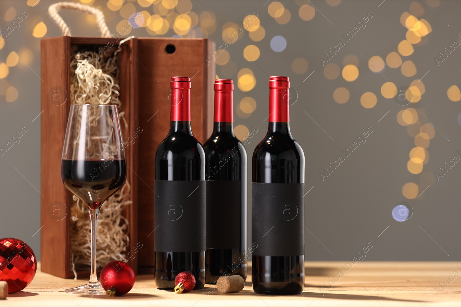 Photo of Bottles of wine, glass, wooden gift boxes, corks and red Christmas balls on table