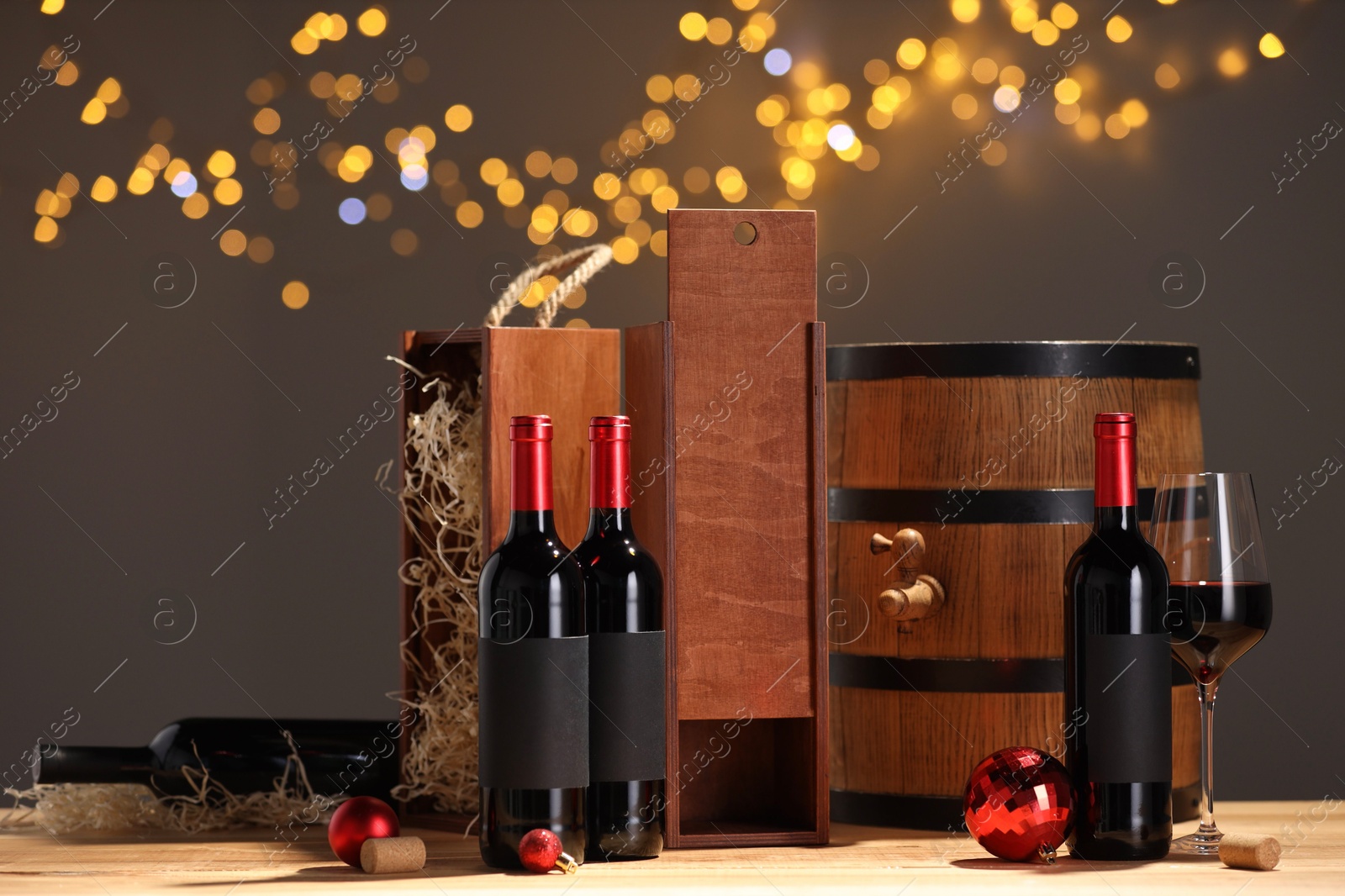 Photo of Bottles of wine, glass, wooden gift boxes, barrel corks and red Christmas balls on table