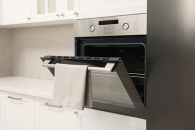 Photo of Open electric oven with towel in kitchen. Cooking appliance