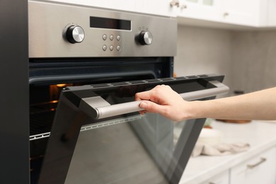 Woman using electric oven in kitchen, closeup