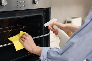 Woman cleaning oven rack with rag and detergent in kitchen, closeup