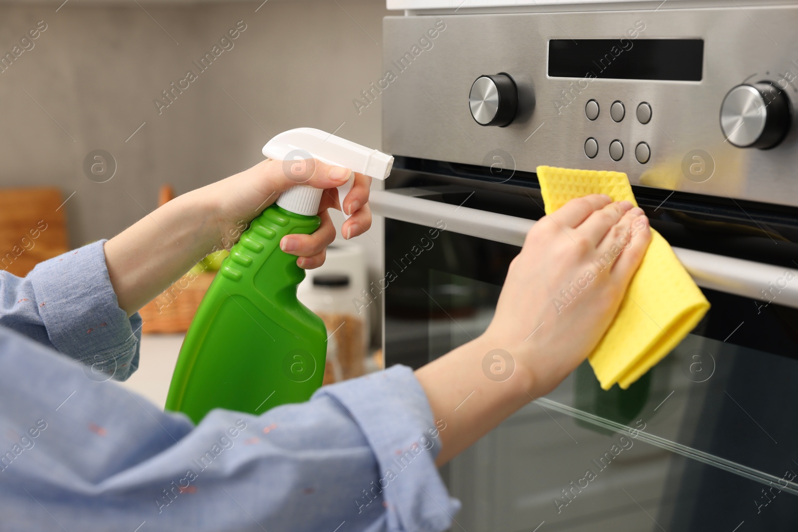 Photo of Woman cleaning electric oven with rag and detergent in kitchen, closeup