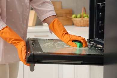 Photo of Woman cleaning oven door with sponge in kitchen, closeup