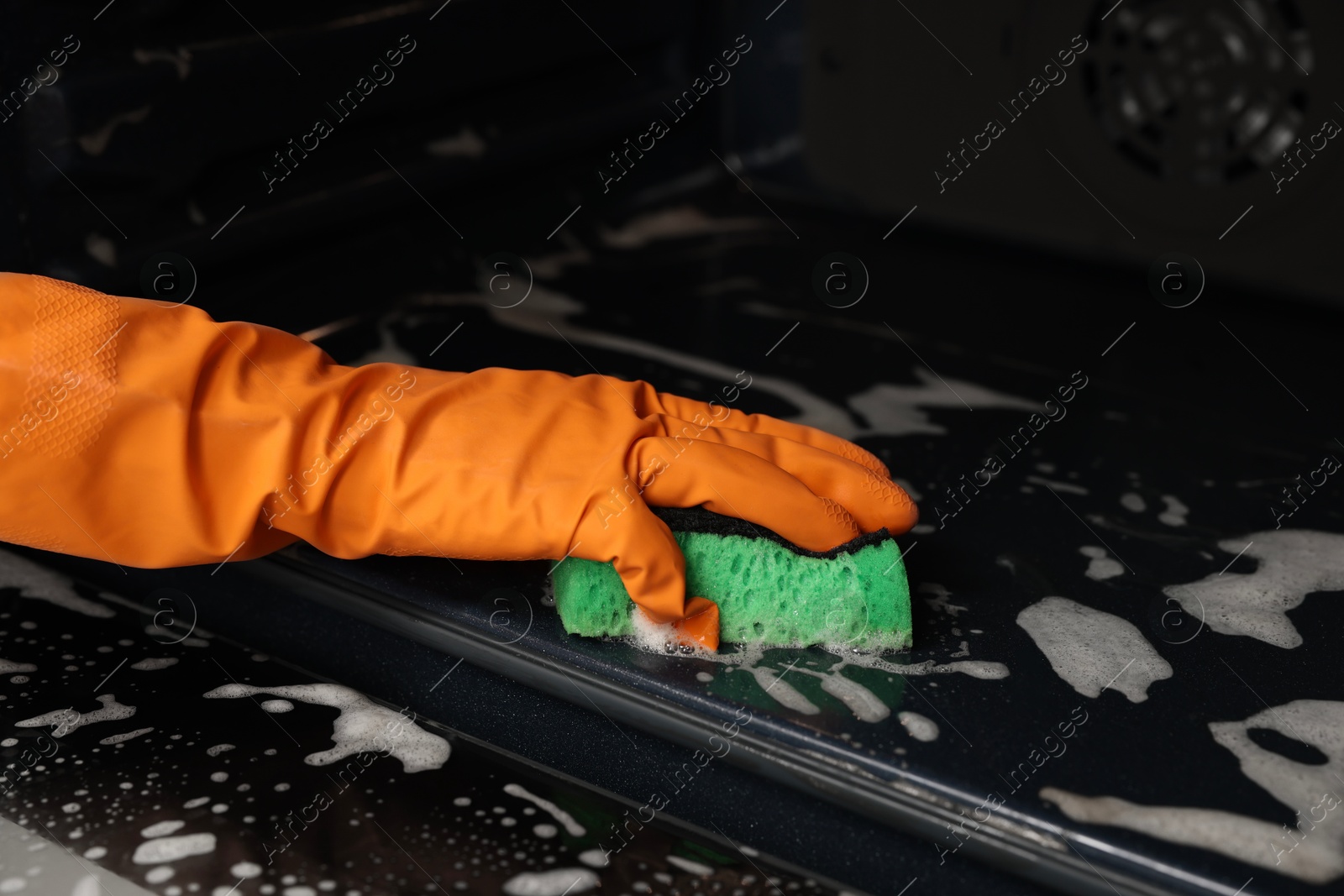 Photo of Woman cleaning oven with sponge, closeup view