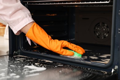 Woman cleaning oven with sponge, closeup view