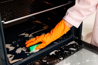 Photo of Woman cleaning oven with sponge, closeup view