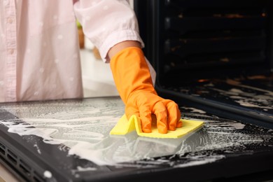 Photo of Woman cleaning oven door with rag, closeup