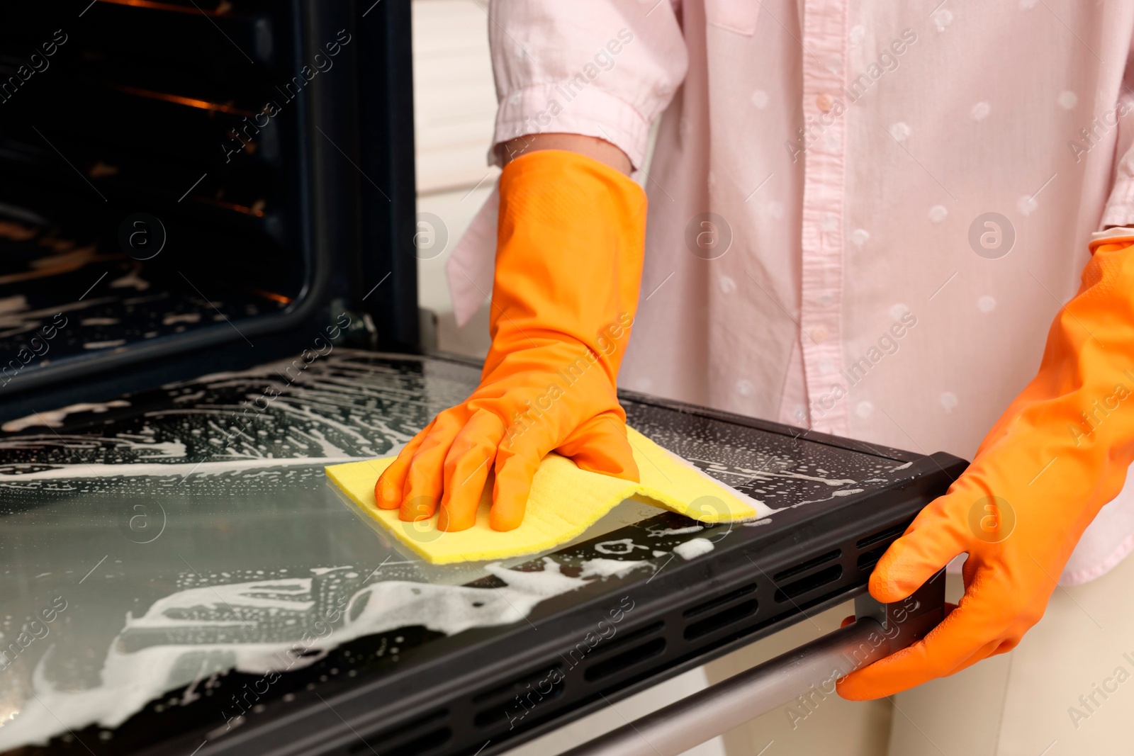 Photo of Woman cleaning oven door with rag, closeup