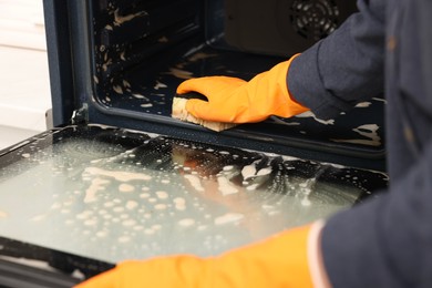 Photo of Woman cleaning oven with sponge in kitchen, closeup