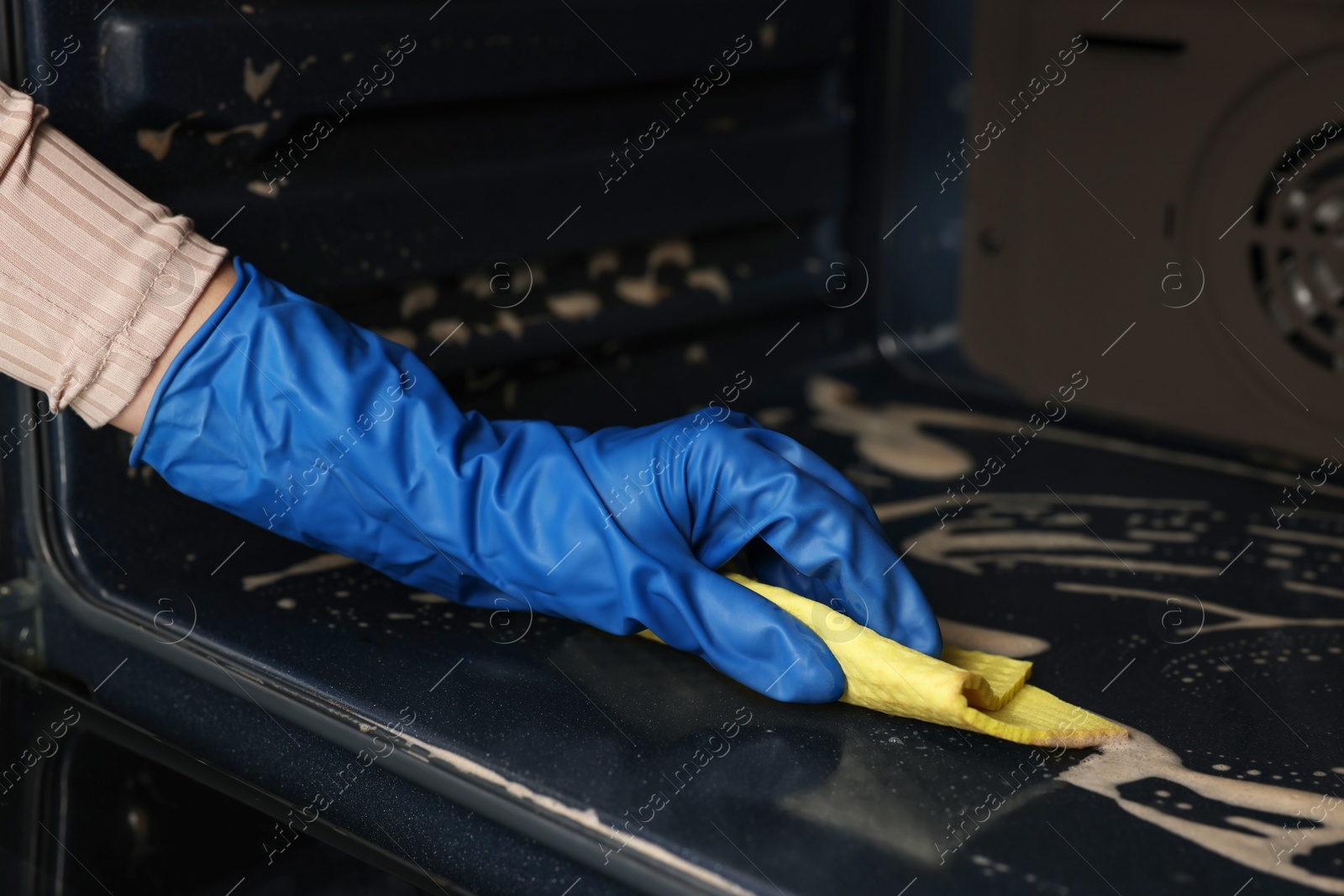 Photo of Woman cleaning oven with rag in kitchen, closeup