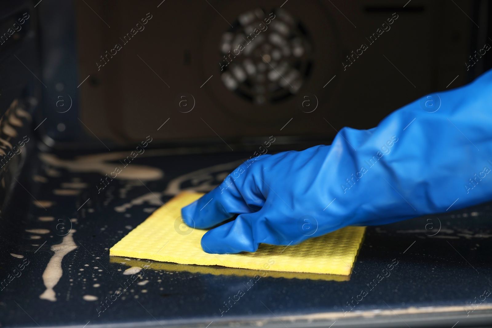 Photo of Woman cleaning oven with rag in kitchen, closeup