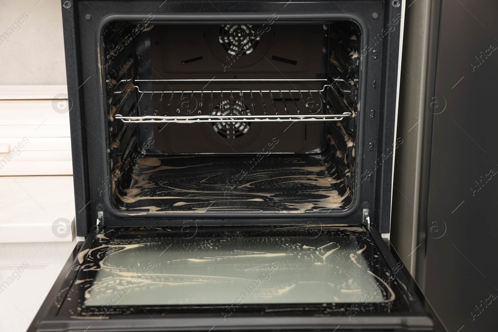 Photo of Open electric oven covered with cleaning foam in kitchen