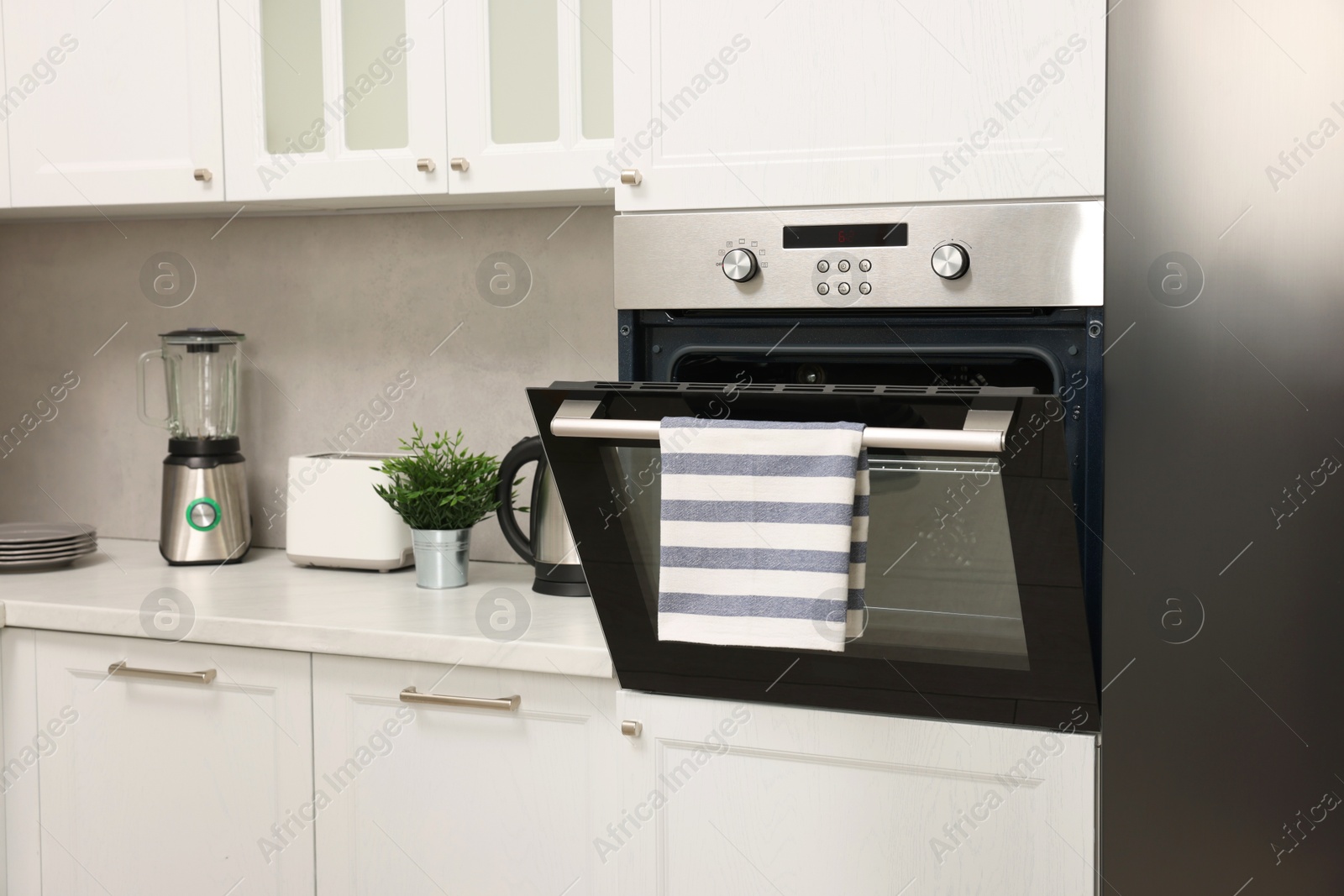 Photo of Open electric oven with striped towel in kitchen. Cooking appliance