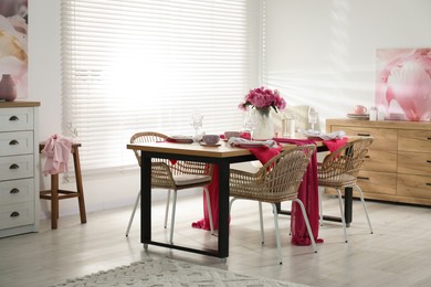 Photo of Pink peonies on table with beautiful setting and rattan chairs in dining room