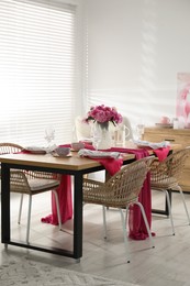 Photo of Pink peonies on table with beautiful setting and rattan chairs in dining room