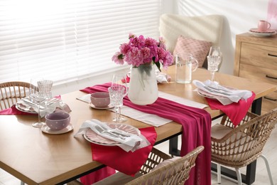 Pink peonies on table with beautiful setting and rattan chairs in dining room