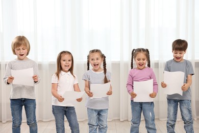Photo of Group of children with sheets of paper singing indoors