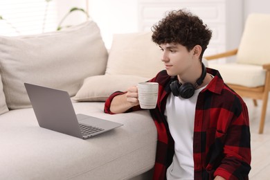 Photo of Teenager with cup of drink working on laptop at home. Remote job