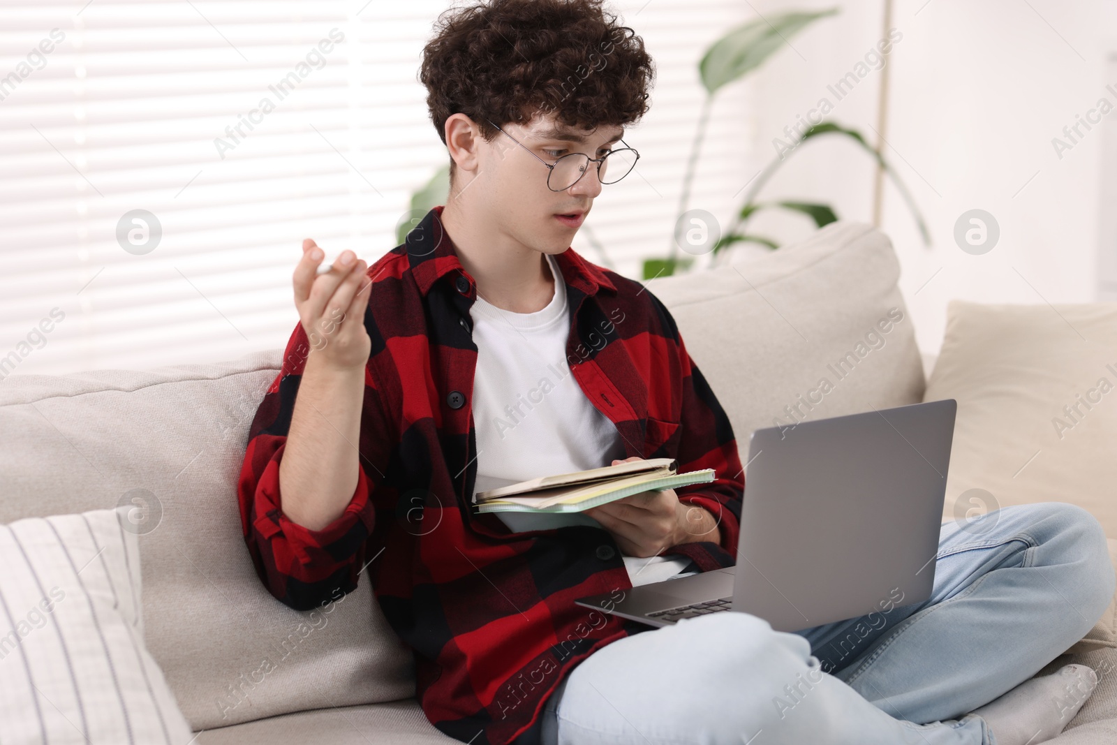 Photo of Teenager with notebooks and pen working on laptop at home. Remote job