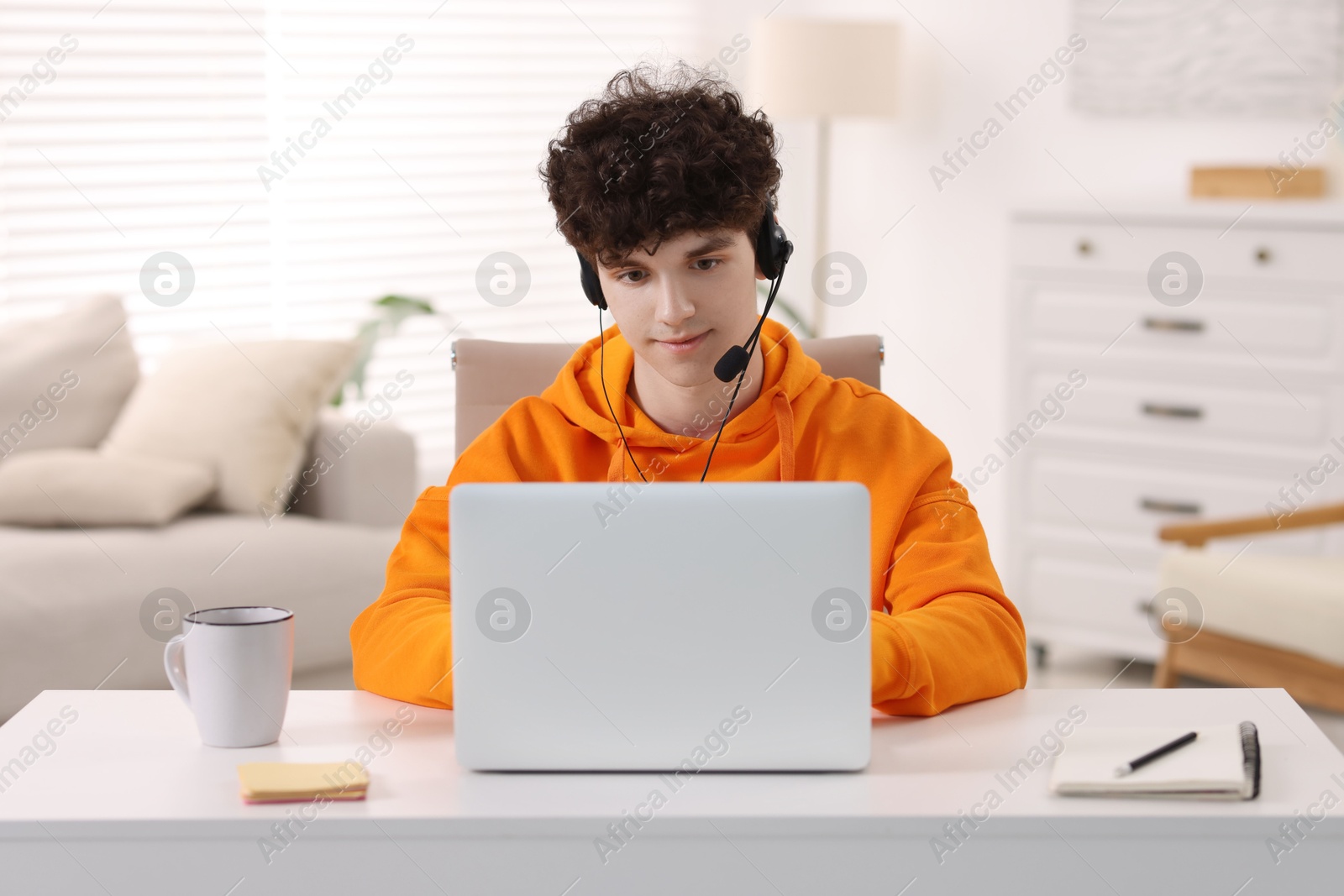 Photo of Teenager in headset working with laptop at home. Remote job