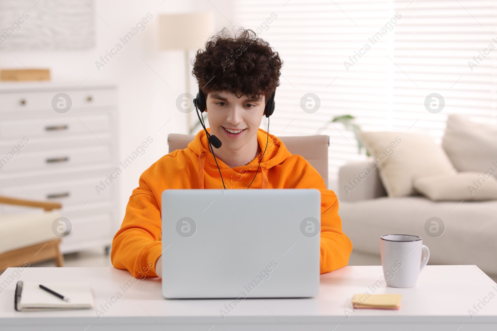 Photo of Teenager in headset working with laptop at home. Remote job