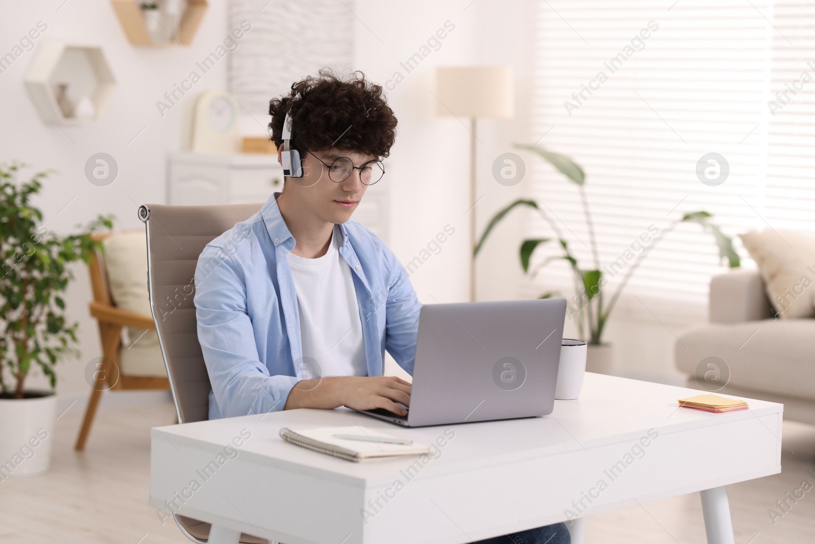 Photo of Teenager in headphones working with laptop at home. Remote job