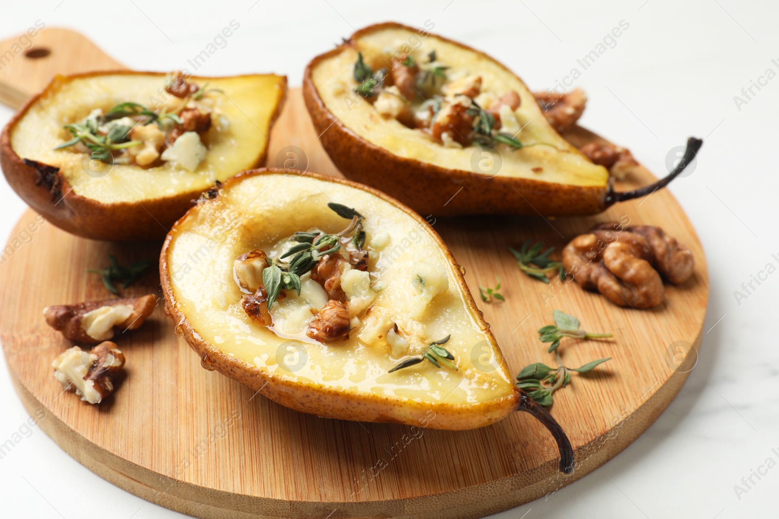 Photo of Tasty baked pears with nuts, blue cheese, thyme and honey dish on white table, closeup