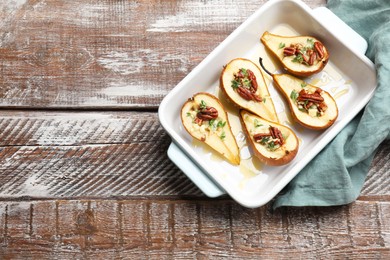 Photo of Tasty baked pears with nuts, blue cheese, thyme and honey in baking dish on wooden table, top view. Space for text