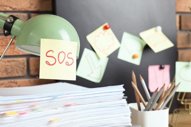 Photo of Sticky note with word SOS on lamp at workplace