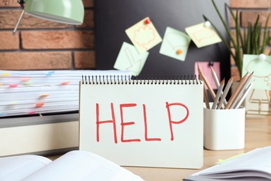 Photo of Notebook with word Help and stationery on wooden table at workplace