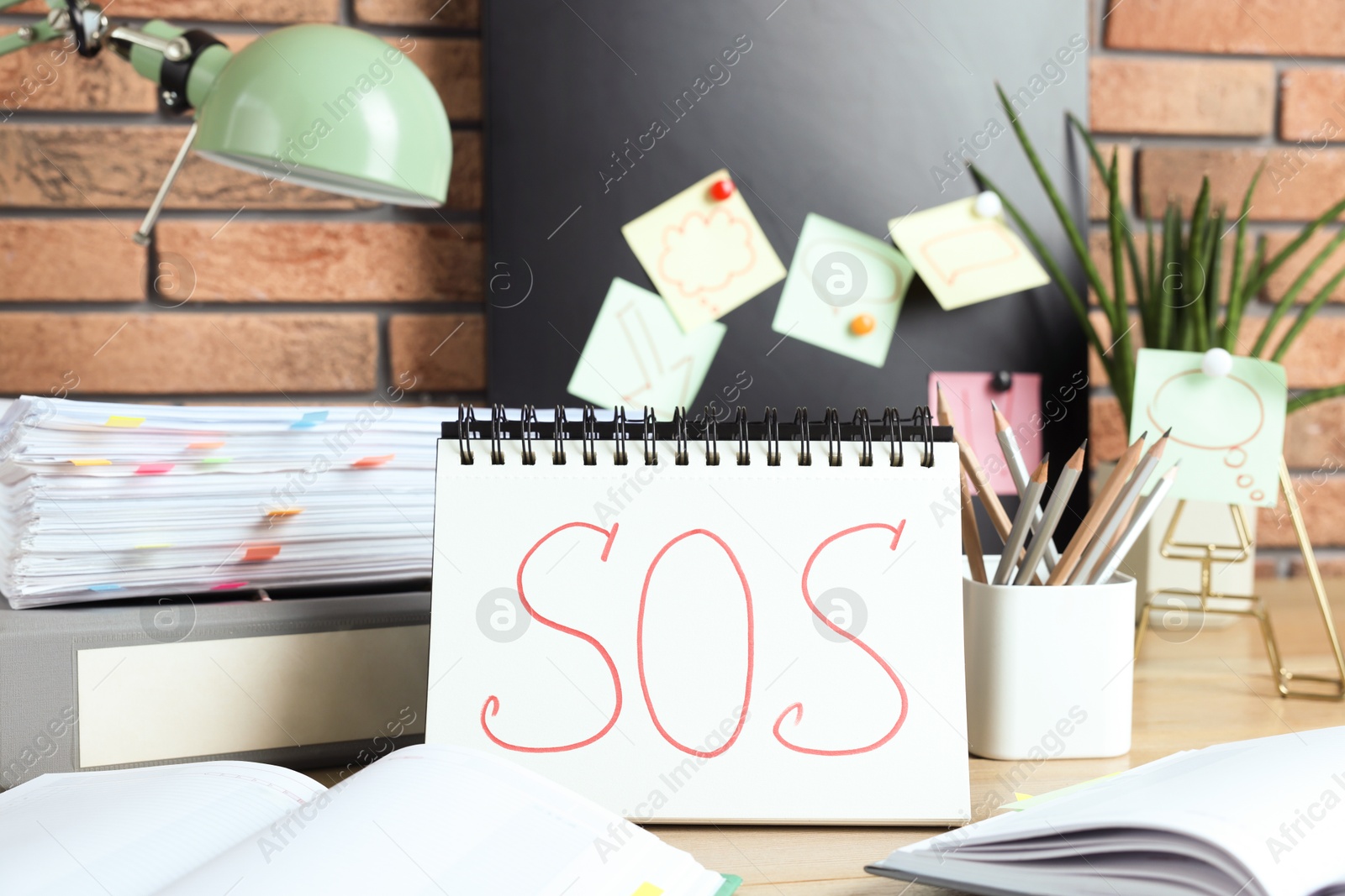 Photo of Notebook with word SOS and stationery on wooden table at workplace