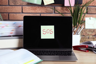 Photo of Sticky note with word SOS, laptop and stationery on wooden table at workplace