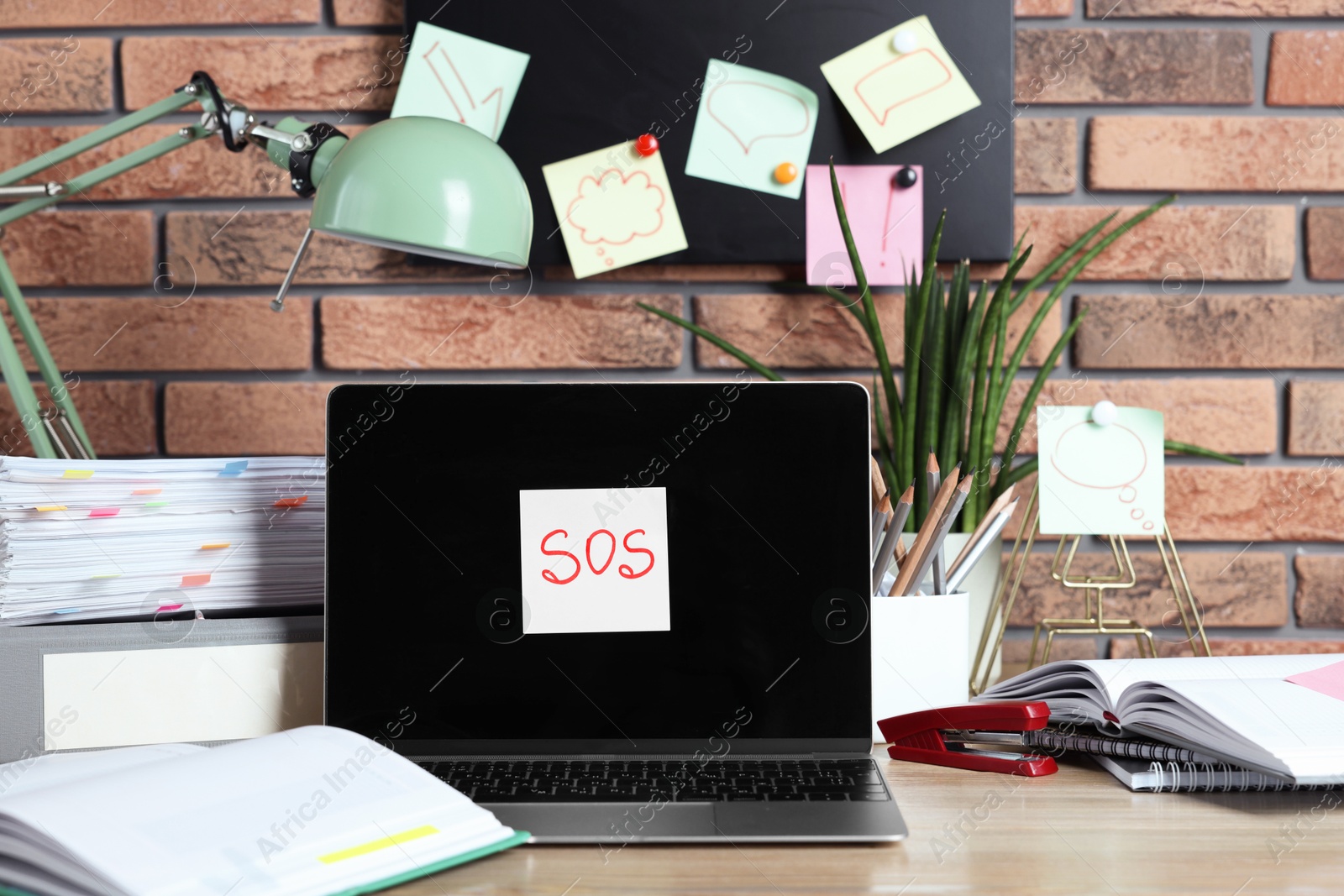 Photo of Sticky note with word SOS, laptop and stationery on wooden table at workplace