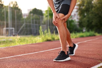 Sportsman with leg injury suffering from knee pain at stadium, closeup. Space for text