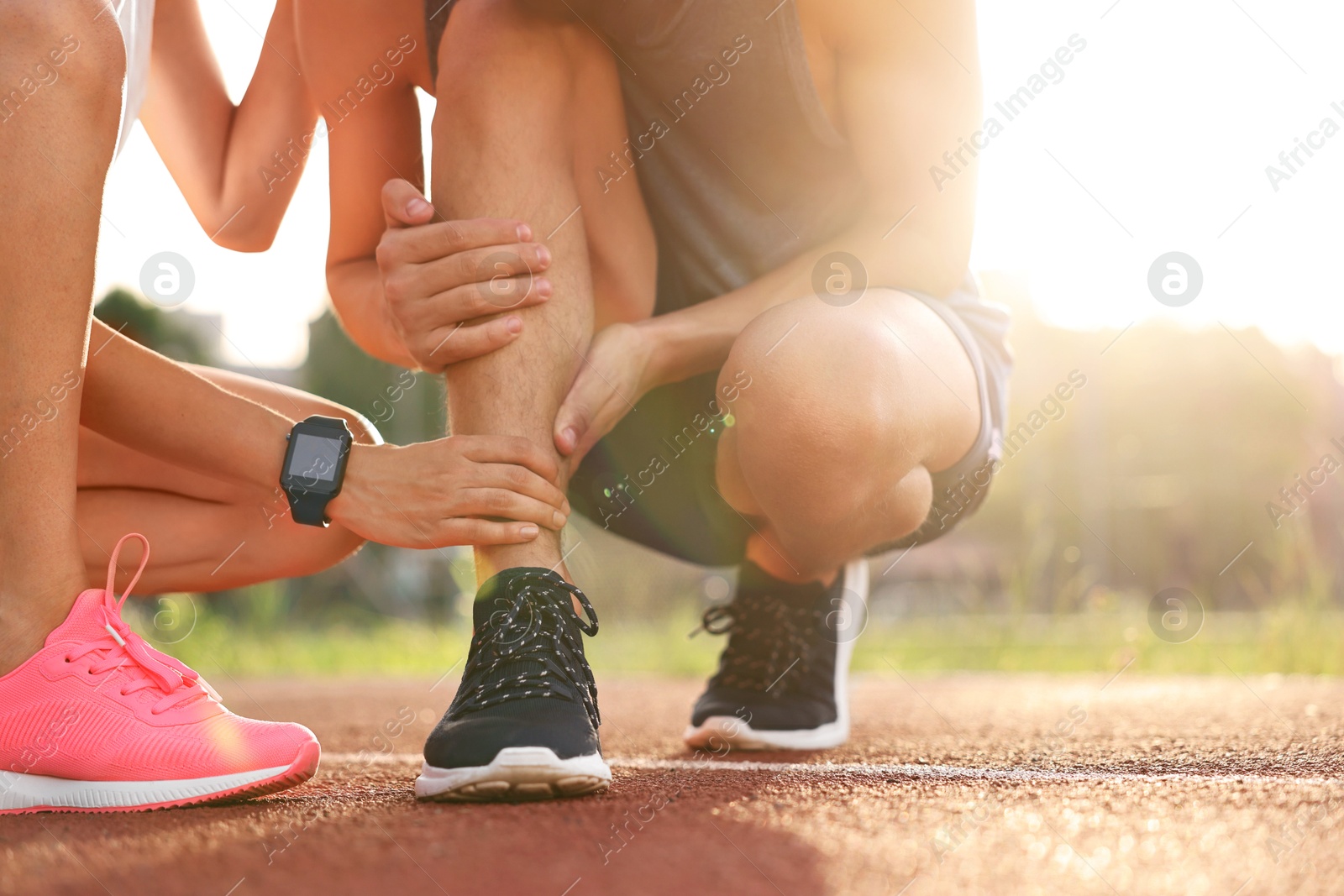 Photo of Sports injury. Woman helping man with leg pain at stadium, closeup