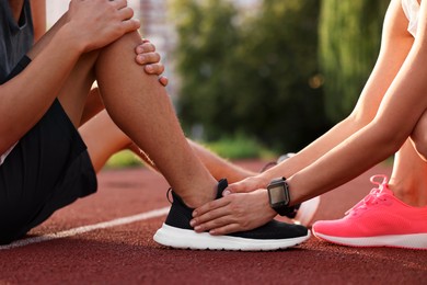 Photo of Sports injury. Woman helping man with leg pain at stadium, closeup