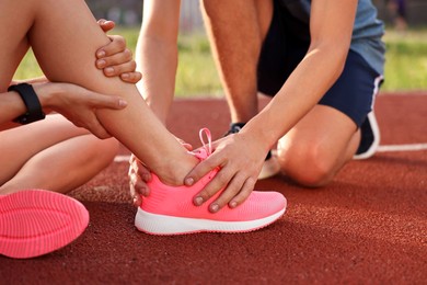 Photo of Sports injury. Man helping woman with leg pain at stadium, closeup