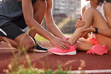 Photo of Sports injury. Man helping woman with leg pain at stadium, closeup