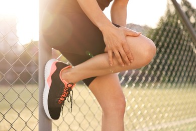 Sportswoman with leg injury suffering from knee pain at stadium, closeup