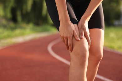 Photo of Sportswoman with leg injury suffering from knee pain at stadium, closeup. Space for text