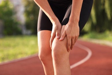 Sportswoman with leg injury suffering from knee pain at stadium, closeup