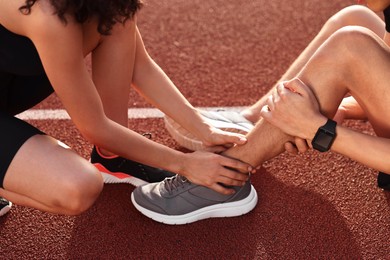 Photo of Sports injury. Woman helping man with leg pain at stadium, closeup