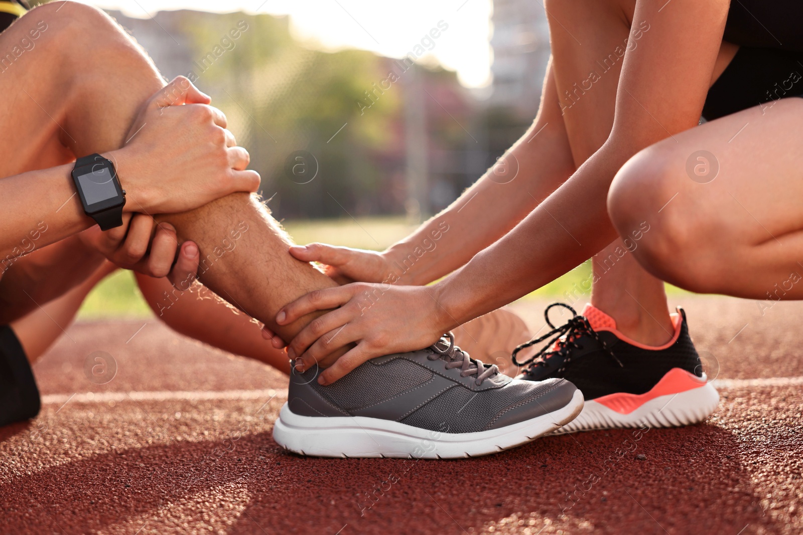 Photo of Sports injury. Woman helping man with leg pain at stadium, closeup