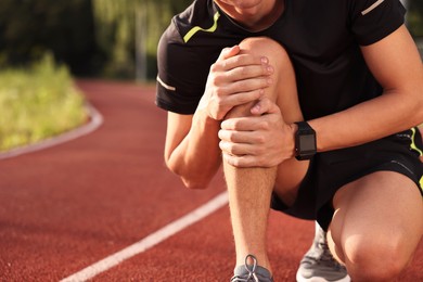 Sportsman with leg injury suffering from knee pain at stadium, closeup. Space for text