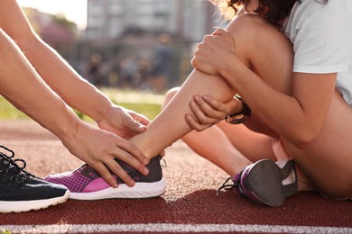 Sports injury. Man helping woman with leg pain at stadium, closeup