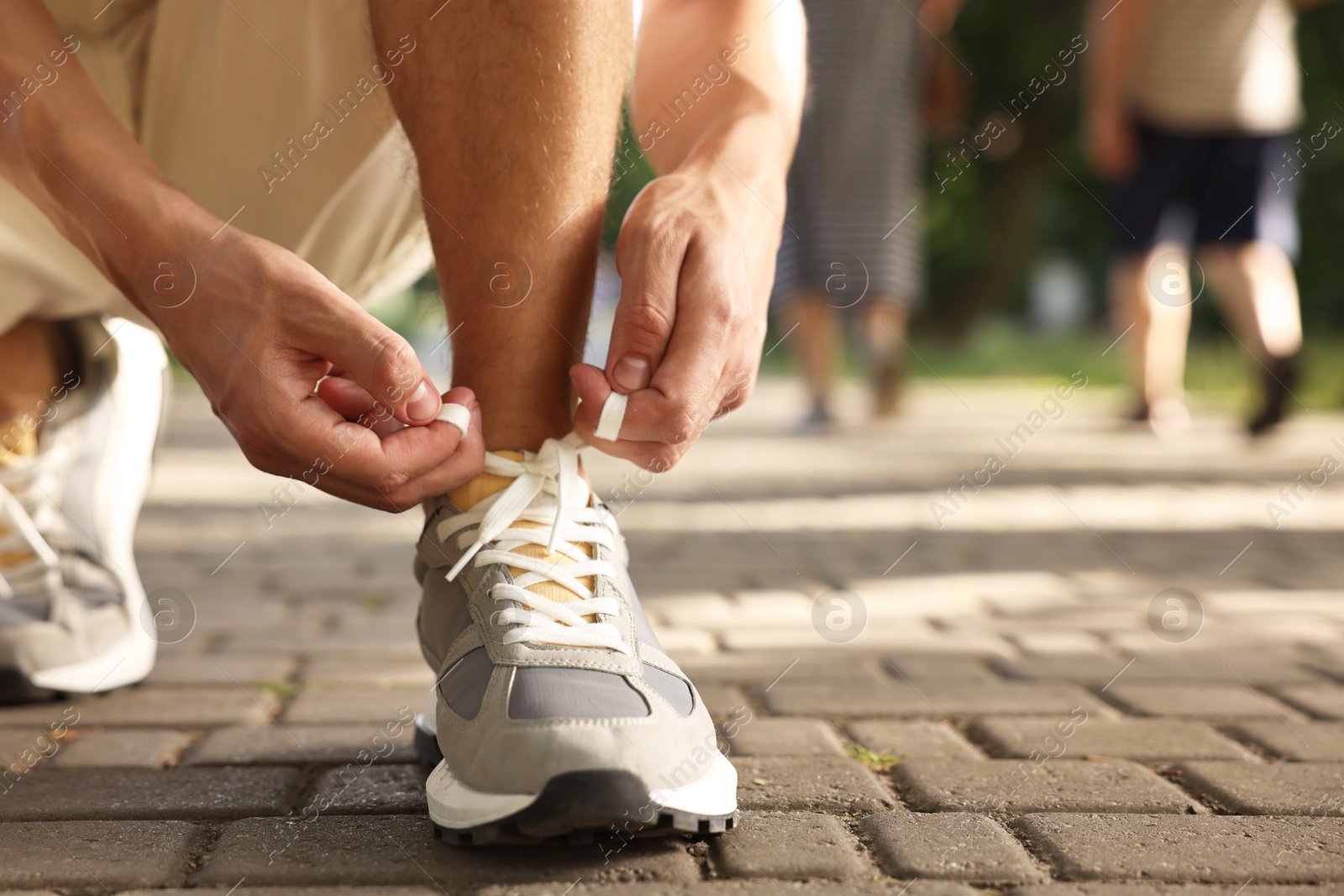 Photo of Man tying shoelace of grey sneaker outdoors, closeup. Space for text