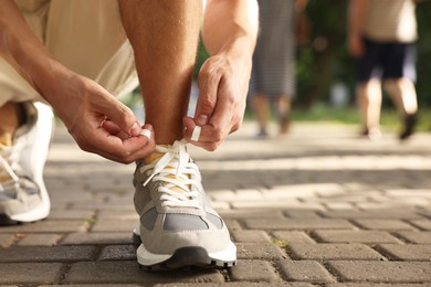 Man tying shoelace of grey sneaker outdoors, closeup. Space for text