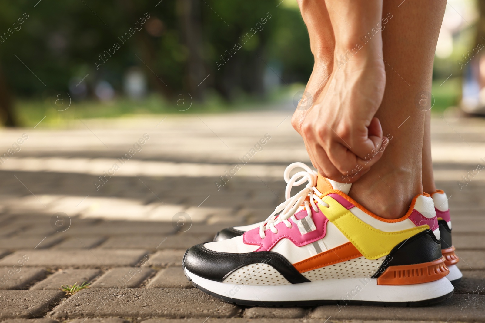 Photo of Woman tying shoelace of sneaker outdoors, closeup. Space for text